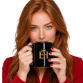Woman in a red blazer holding the EH Crown Signature Black Glossy Mug with gold EH Crown logo.
