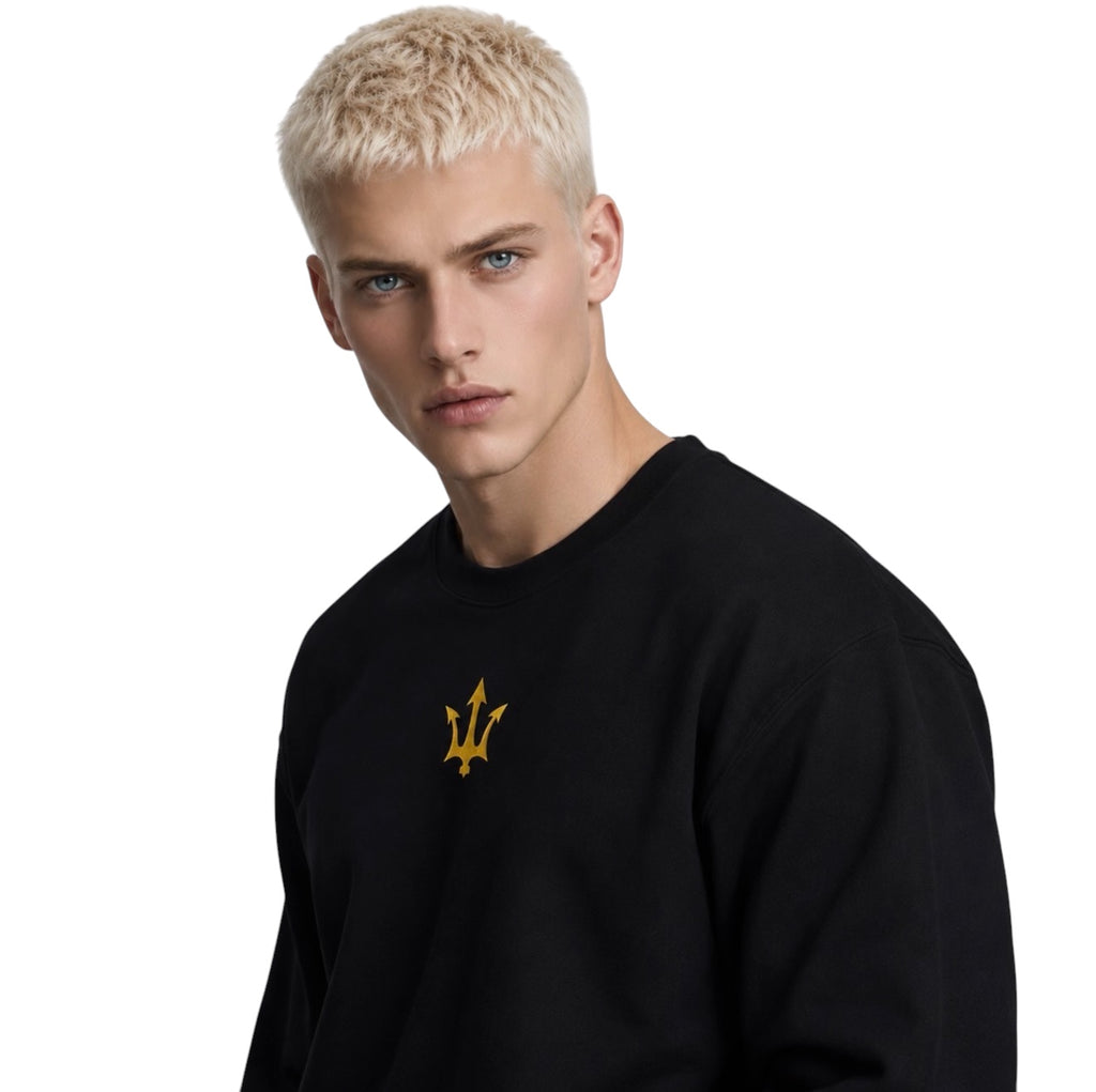 Male model wearing the INSPIRED Sweatshirt in black with gold infinity-trident emblem, angled close-up view.